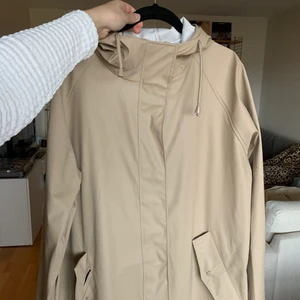 Regnjacka - Beige regnjacka från lager 157, den går ner över knäna på mig som är 167 cm så perfekt för dom som inte använder regnbyxir men vill ha lite mer täckning över benen! Helt oanvänd, nypris 400 kr.