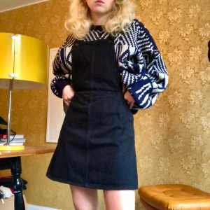 Svart hängselkjol - En svart hängselkjol med dragkedja i midjan och två längdknappar på axelbanden. 