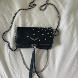 ZADIG VÄSKA - Säljer min superfina Zadig rock heart nano clutch, väl använden med i bra skick. Tycker väskan är så fin men har tyvärr inte så mycket anvädning för den längre. Lite slitningar på hjärtarna och dragkedjan men inget märkvärdigt. Det är den minsta modellen och har ett kort silvrigt band och ett lång som är svart och silvrigt. säljer endast vid bra bud💓 byter gärna mot Zadig Sunny bag, betalar förstår mer om de behövs. BUD JUST NU: 1100