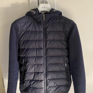 Moncler, Maglia Cardigan - En vår/höstjacka från märket Moncler som även funkar på en sval sommarkväll. Med jackan tillkommer även en luva som enkelt går att sätta på samt ta av. Jackan är stilren och passar till alla outfits. Jackan är köpt i Monclers egna butik i Italien och är i mycket fint skick!   OBS! Köpare står för frakten