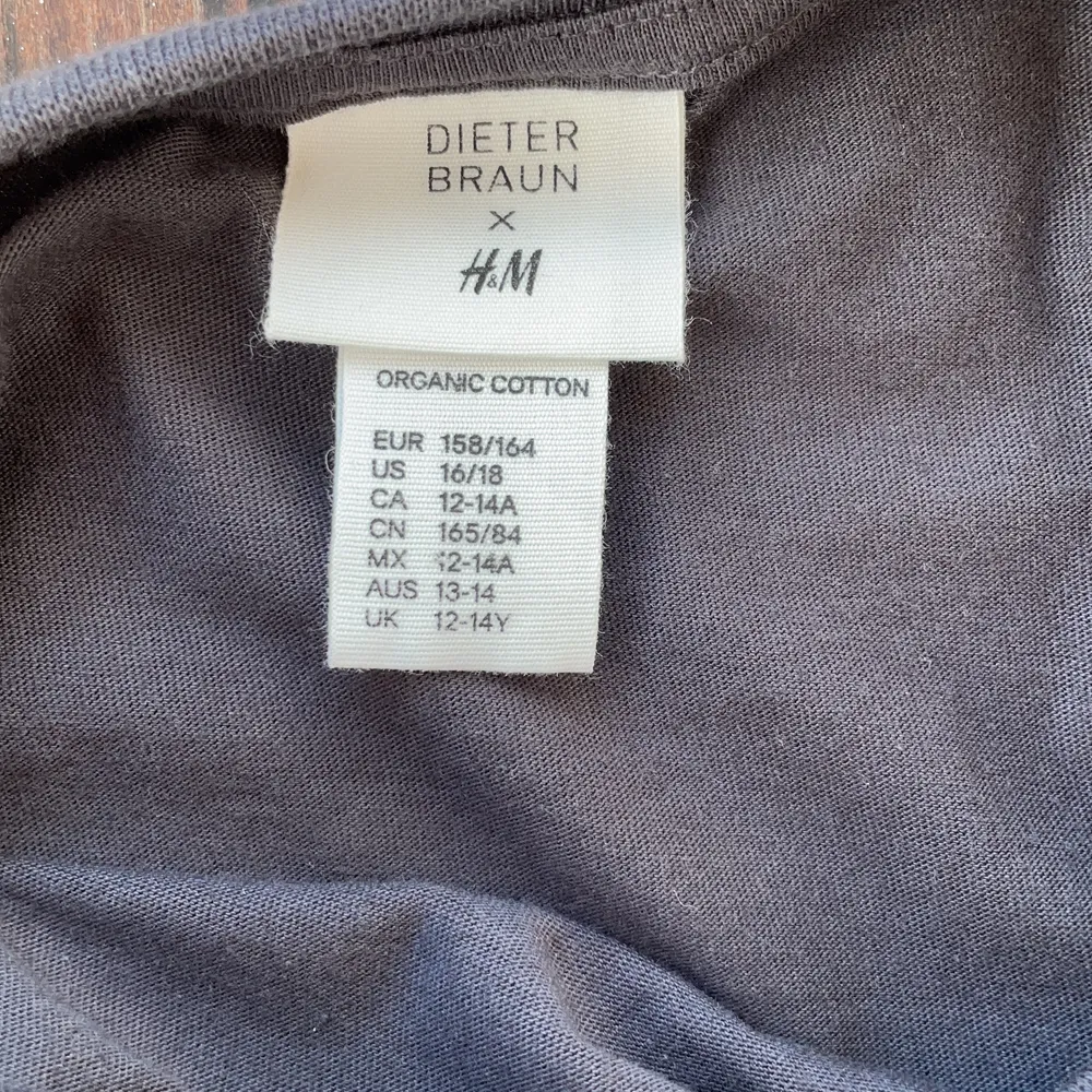 Ett svart linne från H&M med ett färgglatt märke på. Små tofsar på sidorna av ärmarna. . T-shirts.