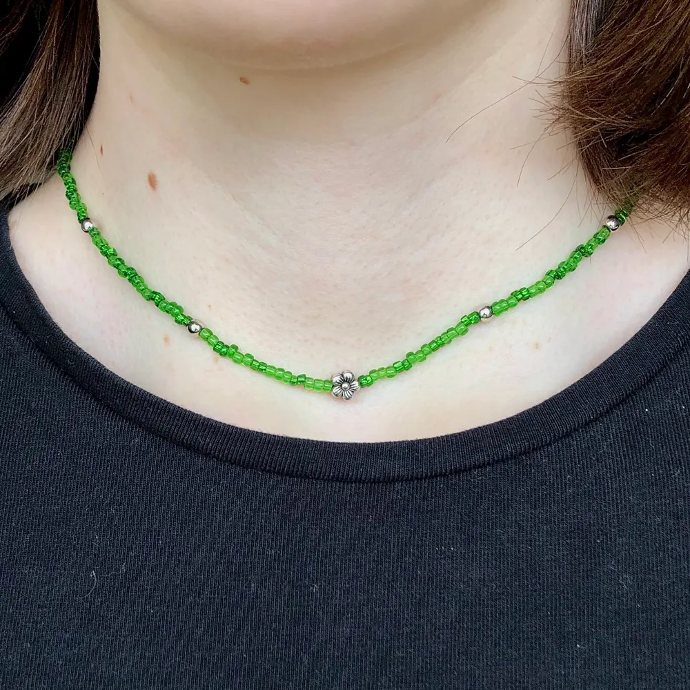 Halsband med seed beads i grönt & har en liten silvrig blomma🌸🌷Gjort med nylontråd och har en förlängning på 3 cm. Säljer för 40kr + 12kr i frakt!. Accessoarer.