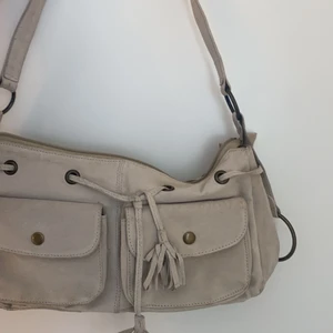 Handväska - Säljer denna supperfina beige/smutsvita handväskan! Ingen aning om märke då den är köpt secondhand och inget märke syns! Köpte för 200kr, säljer för 100kr+frakt! Den har fransdetaljer och massor med förvaring! Vid större intresse blir det budgivning <3