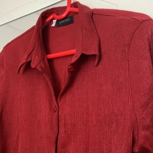 Mörkröd vintage blus - Jag säljer denna mörkröda vintage-blus köpt på second hand! Den har ett stretchigt material som gör att den passar olika kroppsformer. 