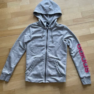 Ljusgrå Adidas zip up hoodie/huvtröja med rosa tryck - Jättefin Adidas zip up hoodie eller huvtröja i ljusgrå färg med rosa tryck☺️ Använd fåtal gånger så är i mycket bra skick och i storlek S dam. Den är ganska tunn med sköna fickor och perfekt att träna i eller ha till vardags:) Kontakta gärna vid frågor, fler bilder eller om du vill köpa💕 Frakt tillkommer på 62kr!