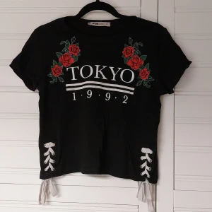 Croptop med text och knytning  - Svart croptop med tryck och vit knytning i sidorna  