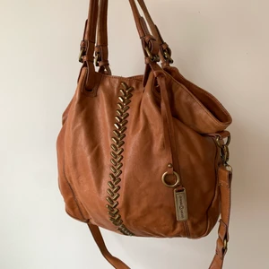 Lucky Brand väska - Brun läderväska från Lucky Brand, köpt i USA. Får plats med extremt mycket i den! Har använts mycket men fortfarande väldigt snygg. Den saknar en nit på framsidan långt ner (se bilden), därav lågt pris. Finns i Linköping om man vill hämta, annars kan jag frakta för 66kr🥰