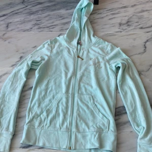 ljus blå JUICY COUTURE kofta  - Hejjj🥰 säljer denna ljus blåa juicy kofta i strl XS på grund av att jag inte använder den längre då den har blivit lite för tight för mig❤️ har använt den ett par fåtals gånger men den är fortfarande i bra skick, på bild två ser du detaljerna av strasset på juicy märket också!🥰 Säljer den för 200kr! Priset kan diskuteras 💖