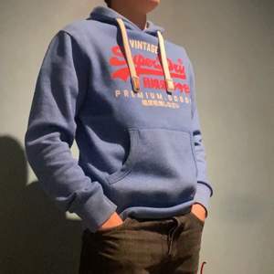 En blå vintage hoodie från märket SUPERDRY, storlek S men passar även längre personer (modellen är 188cm lång)