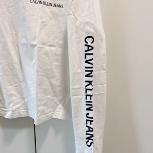 Calvin Klein tröja - En vit Calvin Klein tröja i croppad model med tryck på vänster bröst och på vänster arm. Använd ett par gånger. Fint skick och bra kvalite 🧡