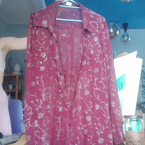 Glittrigarosskjorta - Som tiden lyder. Genomskinlig skjorta i röd och glittriga rosor. Passar XS-L. Haft som kofta, klänning, skjorta och over shirt.