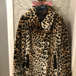 Jofma fuskpäls med skinndetaljer strl 38 - Jättefin fuskpäls i nyskick. Strl 38. Nyskick med fina skinndetaljer runt krage, skärp och knappar.