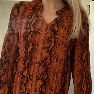 Orm-mönstrad blus - En röd/orange blus med orm-liknande mönster. Liten volangkant uppe vid kragen. Endast använd en gång. Från DenimHunter. Nypris 899.