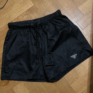 Nylonshorts från Prada storlek S  - Klassiska svarta nylonshorts DAM köpt vintage men i sparsamt skick. Endast loggan som har fått någon ”yta” på sig ( se bild) men syns inte när du när shortsen endast om man tittar NÄRA. Vet ej om de är äkta då det köptes vintage men kommer med tag + lapp. Står L men skulle säga snarare en strl 36. Färg - svart , resår i midjan som kan sjusteras. Skriv vid frågor, mer bilder finns.Jag betalade 950 men tyvärr var dom för små för mig så jag har själv aldrig använt dom, säljer för 400sek då jag vill ha en snabbaffär  + frakt postnord ( frakta lätt 66 sek) 