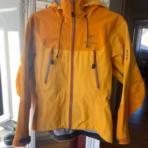 Arcteryx - Arc'teryx Beta AR (orange) - Väldigt bra skick - Beta AR är en mångsidig jacka med hög prestanda. Den är ventilerande, packbar och hållbar. Den är helt vattentät med GORE-TEX XCR vilket är deras mest tåliga version. Den har tecken på slitage med små märken och allmänt slitage genom åren. 