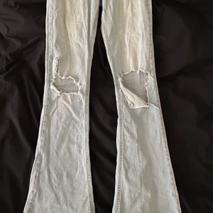 Utsvängda jeans  - Ljusblåa utsvängda jeans ifrån Gina Tricot med till gjorda hål. Frakt tillkommer 