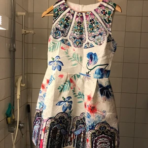 Mönstrad klänning - En kort klänning i vit grund och fina mönster med en dragkedja därbak!