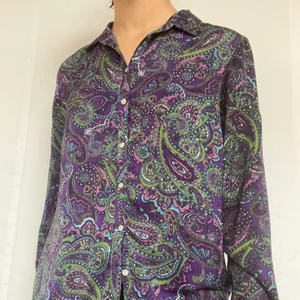 Lila paisley skjorta - Lila paisley skjorta med gröna detaljer. Materialet är mycket likt silke! Perfekt till att ha över tunnare linnen när det varmare vädret kommer. Plagget är i gott defetfritt skick. Köpare står för 57kr spårbar frakt. 