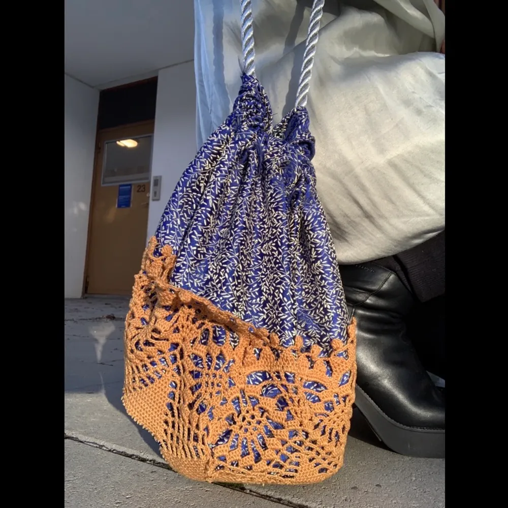 Väska i glansigt blåblommigt tyg med virkade detaljer. . Väskor.