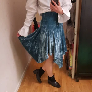 Turkos sammetskjol - Jätteskön sammetskjol som ser blå eller grön ut beroende på ljus. Köpt i Hong Kong och har använts i många år så har några lösa trådar (se bild). Kanten vid midjan ska vikas in och har resår. Om man lägger den platt kan man se att den är fyrkantigt formad. Märkt asiatisk storlek 42 och passar mig som brukar ha strl 36-38. Kan hämtas i Hammarby Sjöstad, annars står köpare för frakten :)