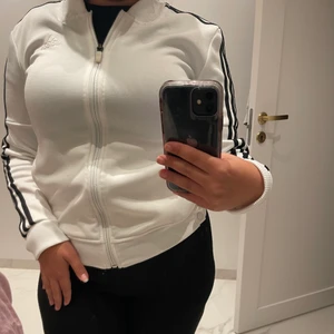 Adida kofta - Vit adidas kofta med svarta sträck. Knappar på båda sidor längst ner.