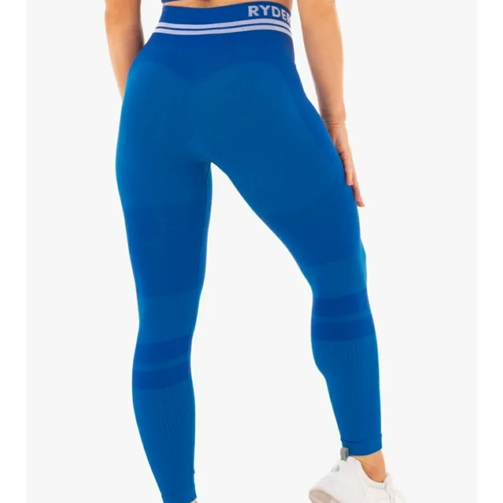 Blå Ryderwear träningstights Namn: The free Seamless high waist leggings Väldigt bra skick. Endast använd två gånger Storlek Small S Nypris är ca 749 kr Samfraktar Detta är hemsidans förklaring: The Freestyle Seamless High Waist Leggings have been perfected for optimal movement, constructed from our unrivalled seamless knit technology for that near naked feel. Whether you’re lounging or lunging, these leggings offer ultimate comfort with a fun, fashionable, body contoured style. The distinctive love heart booty and ribbed contouring flatter your figure, flaunting your glutes and waist. The seamless fabric provides maximum range of motion and agility for dynamic, high-octane home workouts. These luxe leggings also feature a stylish, woven athletic double stripe and can be paired perfectly with the Freestyle Longline Sports Bra. -High waisted legging -Full length -Seamless knit technology -Smooth second skin fit -Supportive seamless rib waistband -Flexibility for maximum movement -Lightweight -Woven Ryderwear logo Recommended for lifestyle, home workouts and gym training. Due to the nature of the soft, seamless fabric we recommend to always wear similar skin tone seamless G-Strings under your seamless leggings and shorts. Model is 167cm tall, she usually wears a size Small and is wearing a size Small. Her waist measures 69cm and her hips measure 84cm. 63% Nylon/24% Polyester/13% Spandex. Farkut & Housut.