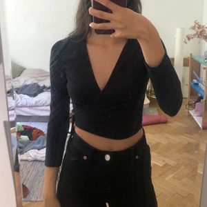 Wrap top från American Apparel - Svart wraptop från American Apparel! Ett av snörena är lite förkortade, men den går fortfarande att stänga bra :)