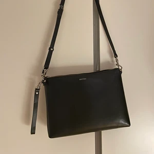 Whyred väska - Stilren svart axelbandsväska i skinn från Whyred (kommer inte ihåg vad modellen heter). 30x23 cm, ena sidan är matt och den andra är glansigt lackad. Finns två små repor på den lackade sidan, annars inget att anmärka på.