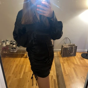 Svart festklänning - Säljer denna fina svart/skimmriga klänningen från Gina Tricot i strl 38. Det går att justera längden på klänningen genom att knyta den på sidorna, samt bestämma urringningen eftersom det finns knappar hela vägen😊 använd 1 gång🖤 