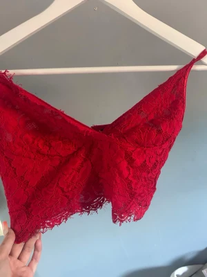 Röd spetsbralette med smala band - Snygg röd bralette i spets med blommigt mönster och smala axelband. Modellen har en omlott-detalj framtill och dekorativ kant nertill. Perfekt för dig som gillar en feminin och trendig look.