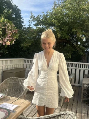 Adooreklänning  - Supersnygg vit kortklänning från adoore med v-ringning och långa, puffiga volangärmar. Klänningen har knappar framtill och ett subtilt blommigt mönster i tyget. Perfekt för sommarens alla tillfällen och ger en romantisk vibe. Skriv för fler bilder!💕