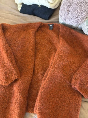 Rostfärgad kofta från Lindex - Mysig och fluffig rostfärgad kofta från Lindex. Koftan har öppen front, lång ärm och är stickad i ett mjukt material som ger en avslappnad look. Perfekt att slänga på sig när det är kyligt ute.