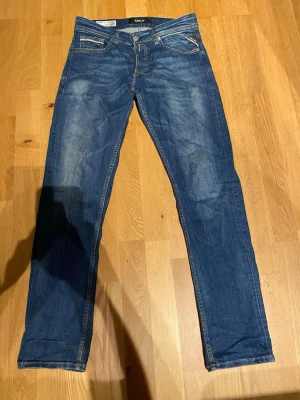 Blå slim fit jeans från Replay Jeans - Snygga blå slim fit jeans från Replay med klassisk femficksdesign och ljusa slitningar framtill. Jeansen har raka ben och kontrastsömmar samt en patch i läder baktill i midjan. Perfekta för en avslappnad och trendig look. Modell grover i storlek 30/32