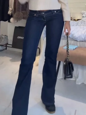 Mörkblå bootcut jeans med låg midja - Snygga mörkblå bootcut jeans med låg midja och klassiska fem fickor. Jeansen har en figurnära passform upptill och utsvängda ben, vilket ger en trendig siluett. Perfekta att styla med sneakers eller boots för en cool look.