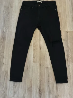 Svarta skinny jeans med slitning - Säljer ett par svarta skinny jeans med hög midja och en snygg slitning på ena benet. Jeansen har klassisk femficksdesign och smal passform hela vägen ner. Perfekta till en trendig streetstyle-look.