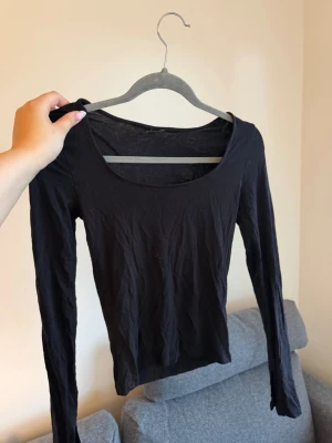Svart långärmad topp - En enkel och stilren svart långärmad topp med rundad urringning. Perfekt basplagg att matcha med olika outfits. Tunn och mjuk i materialet, passar till många tillfällen. Har även slits vid händerna 