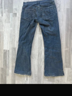Blå bootcut jeans från Authentic - Säljer ett par blå bootcut jeans från Authentic med klassisk femficksdesign och låg midja. Jeansen har en avslappnad passform och är tillverkade i denim med snygg tvätt. Perfekta för en casual look och passar till det mesta.