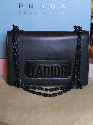 Elegant Black Shoulder Bag – Statement Chain Detail - Sleek and sophisticated black shoulder bag that instantly elevates any outfit. Featuring a structured silhouette, bold raised lettering detail and an eye-catching black chain strap, this piece transitions effortlessly from day to evening. ✨ Structured design that holds its shape beautifully ✨ Black-on-black hardware for a modern, edgy look ✨ Spacious interior with magnetic closure ✨ Perfect for dinners, events, parties or everyday chic styling ‼️One of the magnets lost the leather but is working 