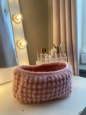 Handvirkad rosa förvaringskorg - Säljer en handvirkad förvaringskorg i mjukt, fluffigt garn. Korgen är ljusrosa och har ett bubbligt mönster på utsidan. Perfekt att ha på sminkbordet eller för småprylar. Den är gjord av akrylgarn blandat med ett mohair-garn💕