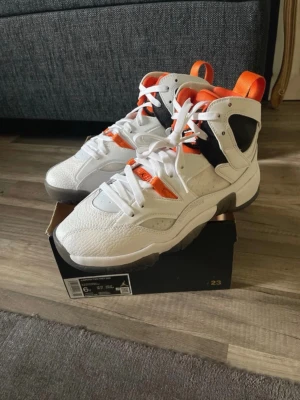 Air Jordan Two Trey vita och orange - Snygga Air Jordan Two Trey sneakers i vitt läder med orange och svarta detaljer. Skorna har högt skaft, klassisk Jumpman-logga på hälen och robust sula. Perfekta för dig som gillar streetwear och vill sticka ut med färg och stil.