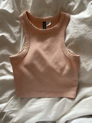Beige ribbad croppad linnetopp - Säljer en beige ribbad croppad linnetopp från H&M Toppen är ärmlös med rund halsringning och har en tight passform som framhäver axlarna. Perfekt att styla med höga jeans eller kjol för en clean och trendig look.