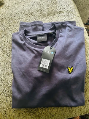 Mörkblå t-shirt från Lyle & Scott - Snygg mörkblå t-shirt från Lyle & Scott med klassisk gul logga broderad på bröstet. T-shirten har rund halsringning och korta ärmar. Tillverkad i mjuk bomull för skön känsla och stilren look.