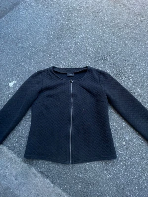 Svart quiltad cardigan från Vila - Snygg svart quiltad cardiganjacka från Vila med dragkedja framtill. Jackan har rund halsringning, lång ärm och ett stilrent, figurnära snitt. Perfekt för lager på lager och enkel att matcha med olika outfits.