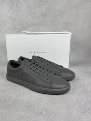Mörkgrå sneakers från Oliver Cabell - Stilrena mörkgrå sneakers från Oliver Cabell i slät läder med matchande grå snörning och sula. Klassisk låg modell med minimalistisk design som passar till det mesta. Perfekta för dig som gillar en clean och modern look.