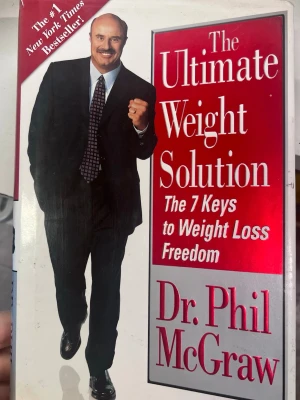 The Ultimate Weight Solution bok - En bok med titeln 'The Ultimate Weight Solution: The 7 Keys to Weight Loss Freedom' av Dr. Phil McGraw. Omslaget är vitt med röd och vit text samt en bild på författaren i kostym. Perfekt för dig som vill läsa om viktminskning och livsstilsförändringar.