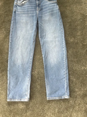 Ljusblå raka jeans med hög midja - Säljer ett par ljusblå jeans med raka ben och hög midja. Jeansen har klassisk femficksdesign och är tillverkade i denim med en snygg tvättad look. Perfekta för en avslappnad och trendig stil.