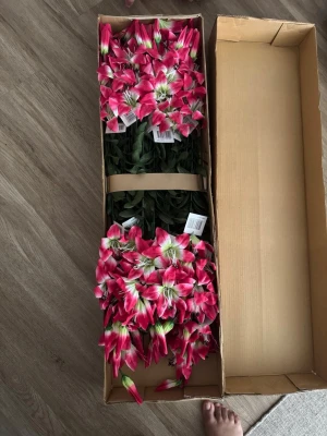 Konstgjorda liljor i ros - Säljer ett gäng konstgjorda liljor i starkt rosa och vitt med gröna blad. Blommorna är gjorda i plast och tyg, perfekta för dekoration hemma eller till event. Kommer i en kartong och är riktigt färgstarka och naturtrogna. Priset för hela kartongen!!!