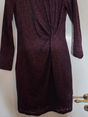 Vinröd spetsklänning från Kappahl - Vinröd långärmad spetsklänning från Kappahl med omlottdetalj framtill. Klänningen har en elegant slits och är tillverkad i ett genombrutet spetsmaterial som ger en lyxig känsla. Perfekt för dig som vill sticka ut med en unik och stilren look.