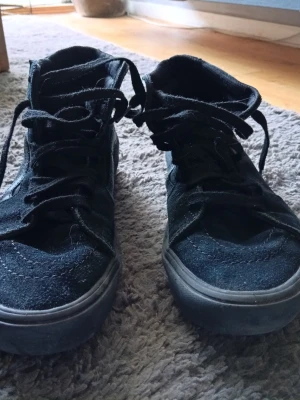 Svarta höga sneakers från Vans - Säljer ett par svarta höga sneakers från Vans med klassisk design. Skorna har mockaliknande material på ovandelen, kraftig sula och snörning hela vägen upp. Perfekta för dig som gillar streetwear och vill ha en tidlös look.