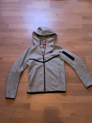 Grå Nike Tech Fleece hoodie - Säljer min grå nike tech i väldigt bra skick, använd max 5 gånger och har inga fläckar. Priset går att diskutera